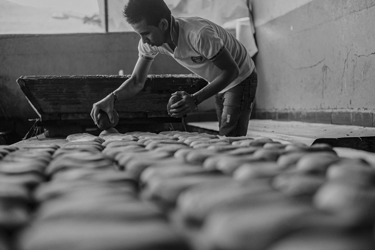 In this action shot, a worker with spiked hair and a popped collar, places newly formed discs of Panela onto a knee high table to harden. In his left hand is the scoop he uses to mold the dozens of disks, which fill the bottom half of the frame. 