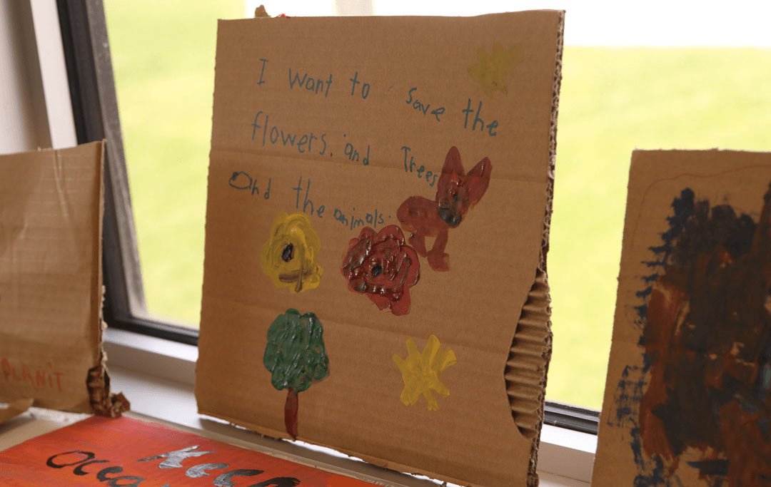 a cardboard piece of art that reads I want to save the trees and flowers and animals