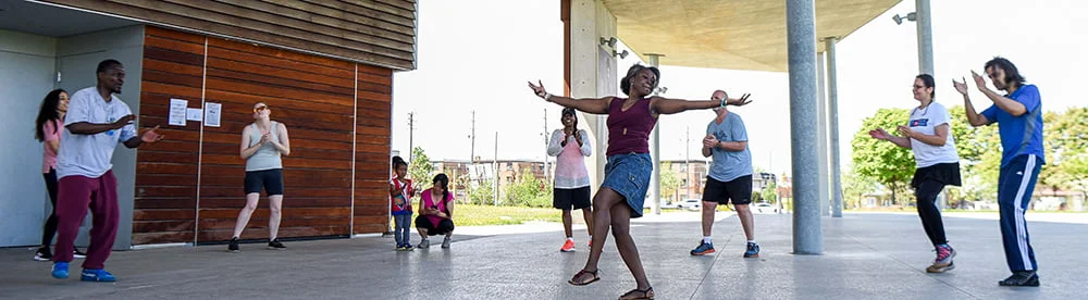 Participants dancing in a circle with one in the middle and others cheering in the background.