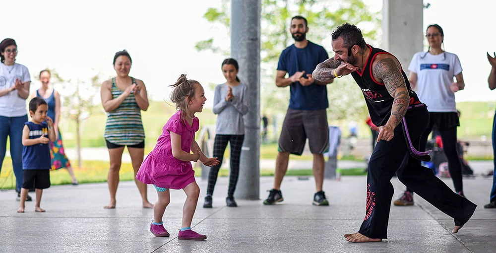 A child and instructor in the middle of the circle practicing Capoeira.